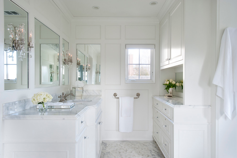 Klassisk inredning av ett en-suite badrum, med ett undermonterad handfat, vita skåp, marmorbänkskiva, vit kakel, stenkakel, vita väggar, marmorgolv och luckor med infälld panel