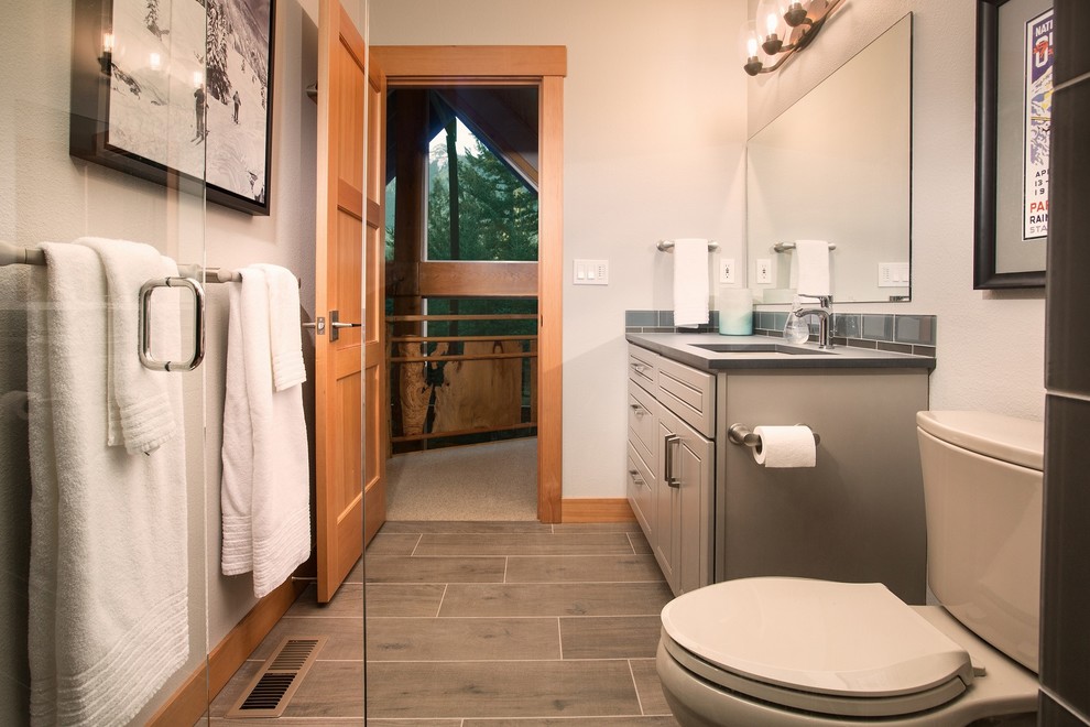 Aménagement d'une salle d'eau montagne de taille moyenne avec un placard avec porte à panneau surélevé, des portes de placard grises, une douche à l'italienne, WC séparés, un carrelage gris, un carrelage en pâte de verre, un mur gris, un sol en carrelage de porcelaine, un lavabo encastré, un plan de toilette en surface solide, un sol gris et une cabine de douche à porte battante.