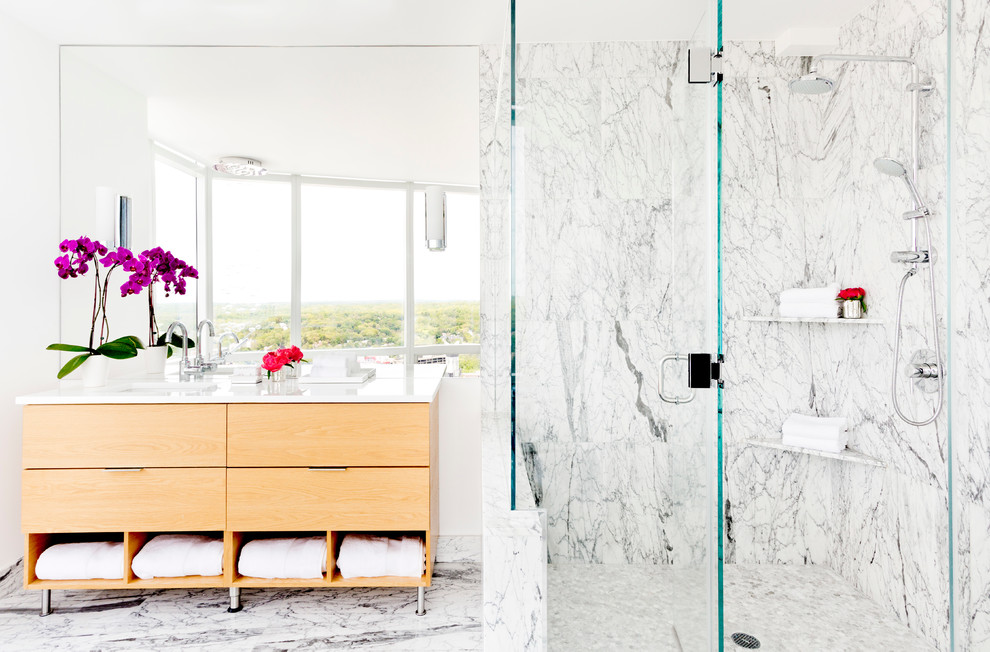 Photo of a contemporary ensuite bathroom in New York with flat-panel cabinets, medium wood cabinets, a freestanding bath, a corner shower, grey tiles, white tiles, stone tiles, white walls, marble flooring, a submerged sink, engineered stone worktops and a hinged door.