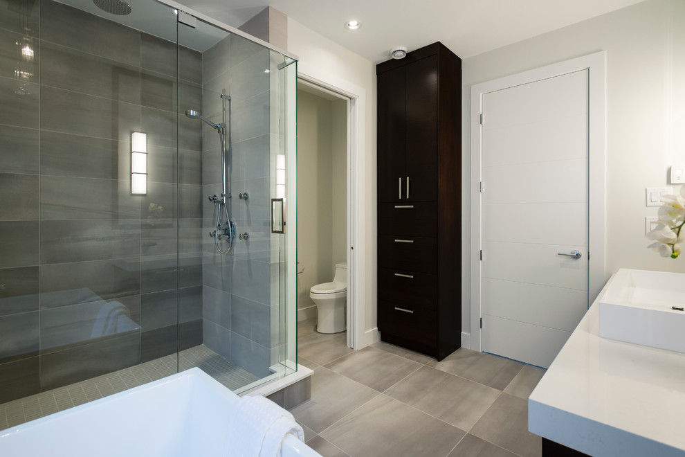 This is an example of a medium sized ensuite bathroom in Vancouver with freestanding cabinets, dark wood cabinets, a freestanding bath, a walk-in shower, a one-piece toilet, grey tiles, stone tiles, white walls, slate flooring, a trough sink and marble worktops.