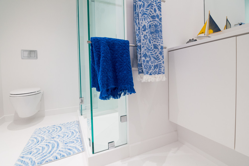 Foto på ett mellanstort funkis vit en-suite badrum, med släta luckor, vita skåp, en hörndusch, en vägghängd toalettstol, vit kakel, vita väggar, ett integrerad handfat, bänkskiva i akrylsten, vitt golv och dusch med gångjärnsdörr