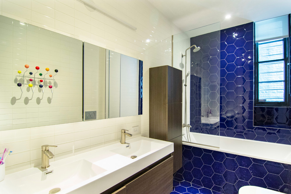 Large urban kids' blue tile and porcelain tile ceramic tile and blue floor drop-in bathtub photo in New York with flat-panel cabinets, dark wood cabinets, a wall-mount toilet, white walls, an integrated sink, solid surface countertops and white countertops