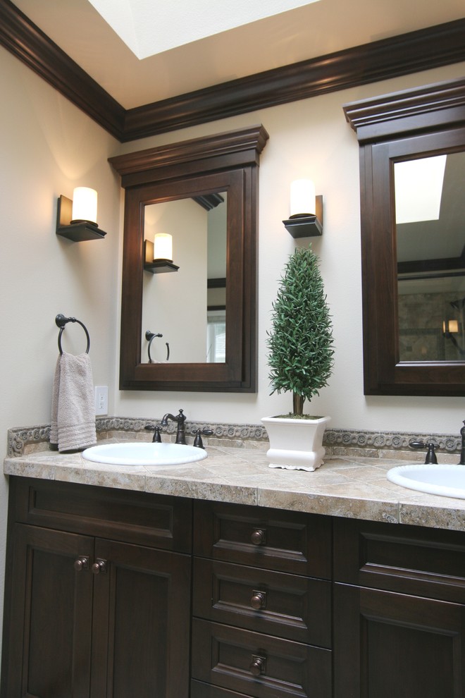 シアトルにある中くらいなトランジショナルスタイルのおしゃれな浴室 (オーバーカウンターシンク、落し込みパネル扉のキャビネット、濃色木目調キャビネット、タイルの洗面台、ベージュのタイル、石タイル、白い壁) の写真