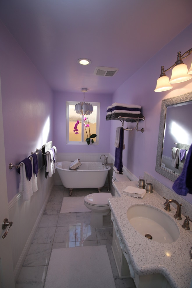 Cette photo montre une salle d'eau chic de taille moyenne avec un lavabo encastré, un placard à porte affleurante, des portes de placard blanches, un plan de toilette en quartz modifié, une baignoire sur pieds, WC séparés, un carrelage gris, un carrelage de pierre, un mur violet et un sol en marbre.