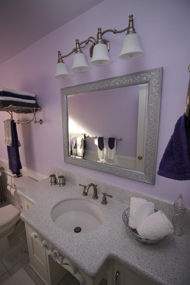 Klassisk inredning av ett mellanstort badrum med dusch, med ett undermonterad handfat, luckor med profilerade fronter, vita skåp, bänkskiva i kvarts, ett badkar med tassar, en toalettstol med separat cisternkåpa, grå kakel, stenkakel, lila väggar och marmorgolv
