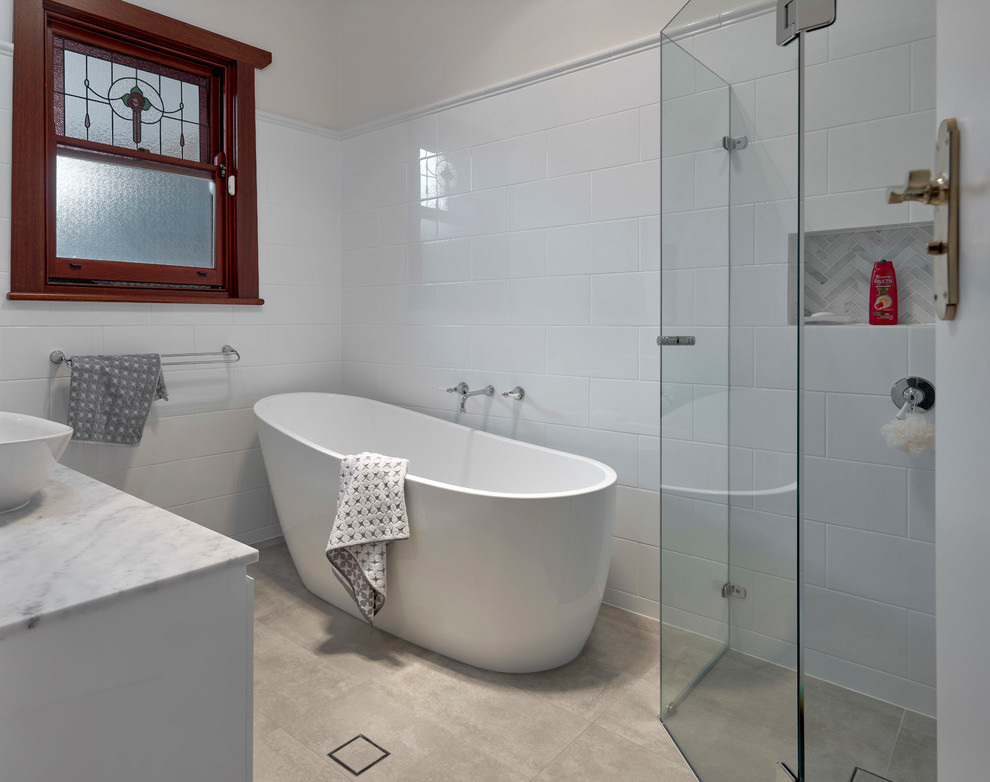 Inspiration for a small traditional ensuite bathroom in Other with white cabinets, porcelain flooring, flat-panel cabinets, a freestanding bath, a corner shower, white tiles, porcelain tiles, white walls, a vessel sink, marble worktops, grey floors, a hinged door and multi-coloured worktops.