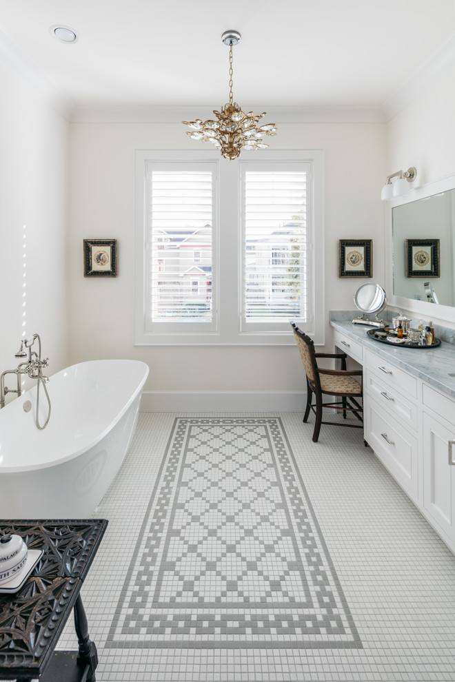 Aménagement d'une salle de bain classique avec un placard à porte shaker, des portes de placard blanches, une baignoire indépendante, un mur blanc, un lavabo encastré et un sol blanc.