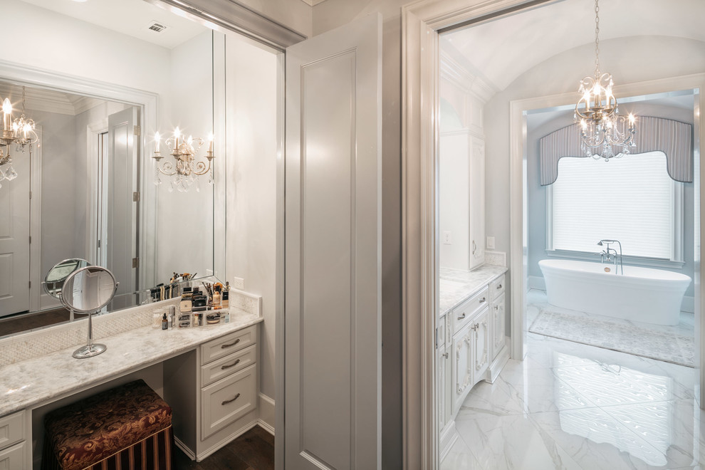 This is an example of an expansive traditional ensuite bathroom in Houston with shaker cabinets, white cabinets, a freestanding bath, white walls, marble flooring, a submerged sink, marble worktops, white floors, double sinks, a built in vanity unit and a vaulted ceiling.