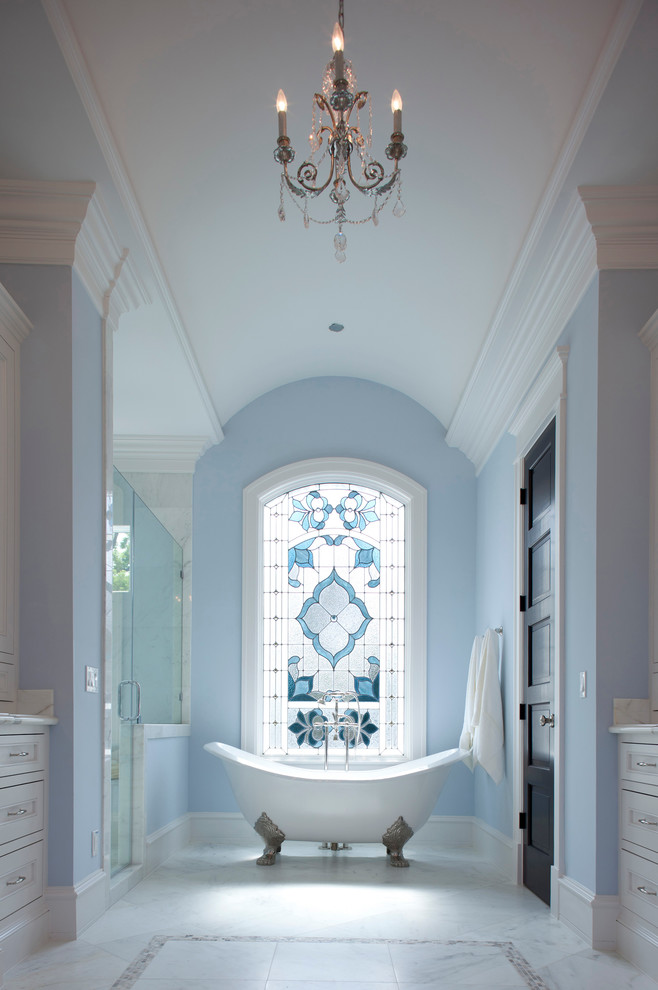 Exemple d'une grande douche en alcôve principale chic avec une baignoire sur pieds, un placard avec porte à panneau encastré, des portes de placard blanches, un carrelage blanc, un mur bleu, un sol en marbre, un plan de toilette en marbre, un sol blanc, une cabine de douche à porte battante, un plan de toilette blanc, une fenêtre et meuble double vasque.