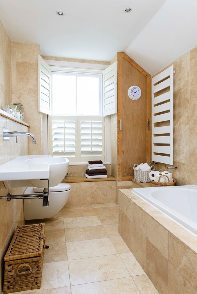 Bild på ett litet maritimt badrum, med ett väggmonterat handfat, ett platsbyggt badkar och travertinkakel
