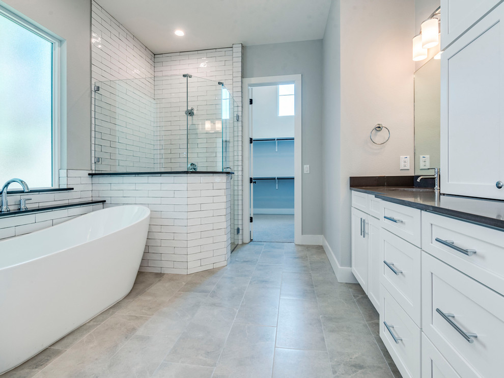 Inspiration for an expansive traditional ensuite bathroom in Dallas with shaker cabinets, white cabinets, a freestanding bath, a corner shower, a one-piece toilet, white tiles, metro tiles, grey walls, ceramic flooring, a submerged sink, engineered stone worktops, grey floors, a hinged door and black worktops.