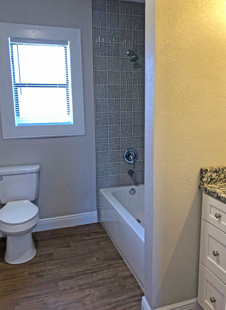 Idéer för att renovera ett litet amerikanskt grå grått badrum för barn, med skåp i shakerstil, vita skåp, ett badkar i en alkov, en dusch/badkar-kombination, en toalettstol med separat cisternkåpa, grå kakel, keramikplattor, grå väggar, klinkergolv i porslin, ett undermonterad handfat, granitbänkskiva och brunt golv