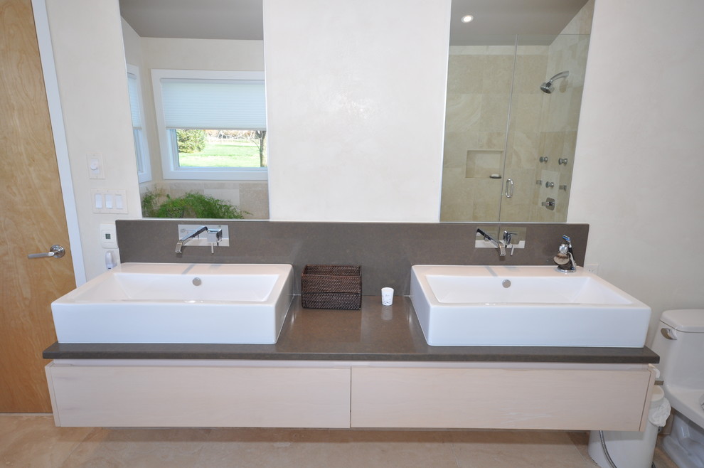 Photo of an expansive modern ensuite bathroom in Philadelphia with a vessel sink, flat-panel cabinets, light wood cabinets, quartz worktops, a corner bath, an alcove shower, a one-piece toilet, beige tiles, stone tiles, beige walls and marble flooring.