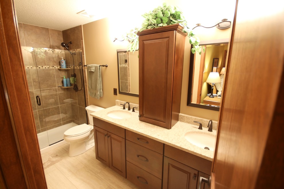This is an example of a medium sized traditional ensuite bathroom in Other with medium wood cabinets, ceramic flooring, raised-panel cabinets, a two-piece toilet, beige tiles, ceramic tiles, beige walls, a submerged sink, engineered stone worktops and an alcove shower.