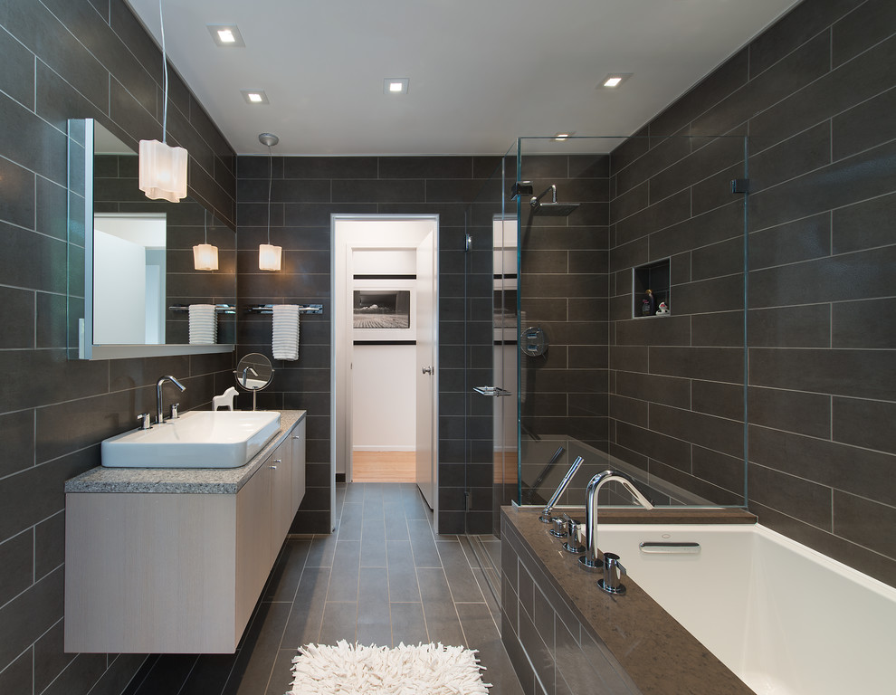 Inredning av ett modernt en-suite badrum, med släta luckor, skåp i ljust trä, ett undermonterat badkar, en kantlös dusch, brun kakel, ett fristående handfat och dusch med gångjärnsdörr