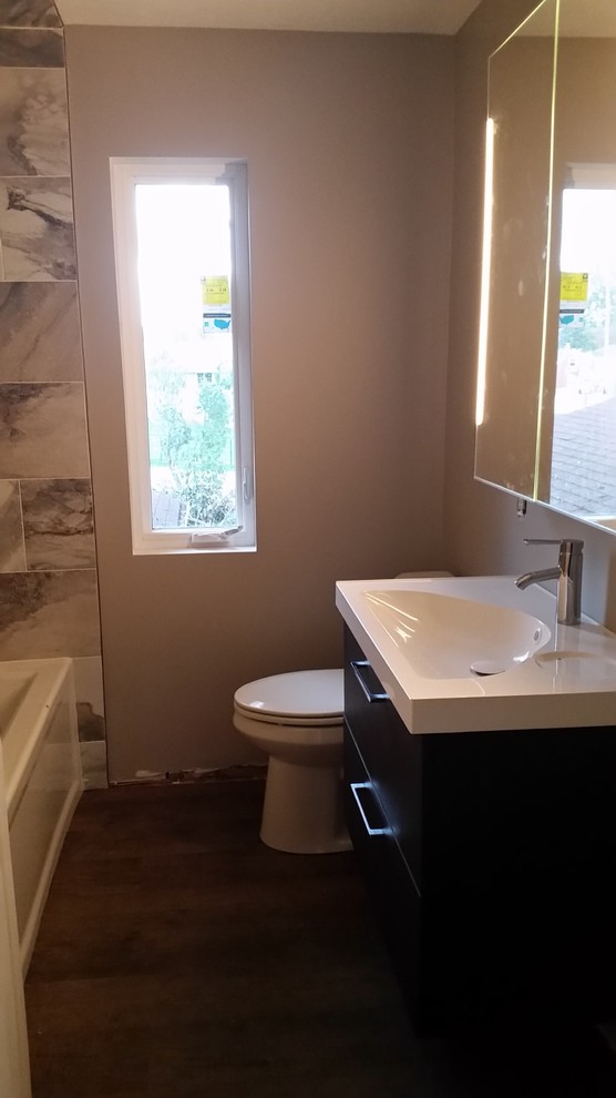 Photo of a small traditional bathroom in Other with flat-panel cabinets, brown cabinets, an alcove bath, a shower/bath combination, a two-piece toilet, grey tiles, porcelain tiles, beige walls, vinyl flooring, an integrated sink and solid surface worktops.