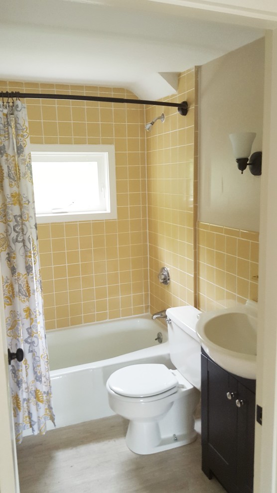Cette image montre une petite salle de bain principale marine avec un placard avec porte à panneau encastré, des portes de placard noires, une baignoire posée, un combiné douche/baignoire, WC à poser, un carrelage jaune, des carreaux de porcelaine, un mur beige, parquet clair et une vasque.