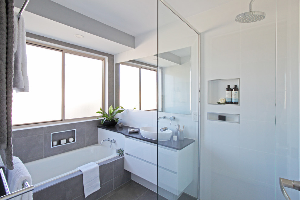 Inspiration for a small contemporary family bathroom in Brisbane with flat-panel cabinets, white cabinets, a built-in bath, a corner shower, a two-piece toilet, white tiles, ceramic tiles, white walls, terracotta flooring, a vessel sink, engineered stone worktops, grey floors, a hinged door and black worktops.
