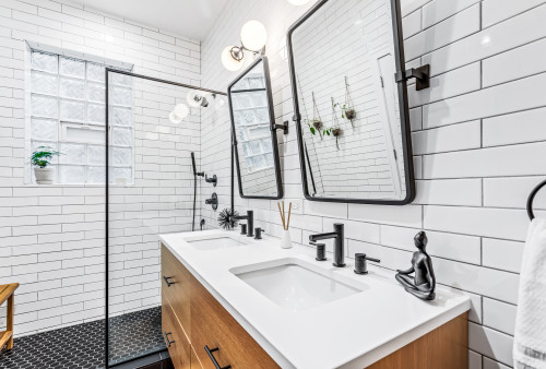 Modern bathroom with white subway tile walls, dual rectangular mirrors, wood vanity cabinets with white countertop, matte black faucets, and walk-in shower with glass partition.