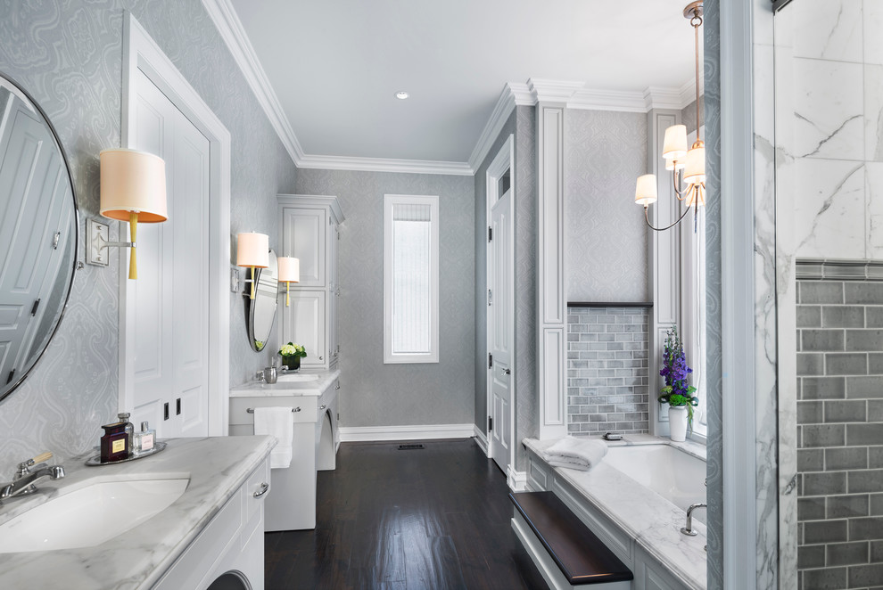 Aménagement d'une douche en alcôve classique avec des portes de placard blanches, une baignoire encastrée, un mur gris, parquet foncé et un lavabo encastré.