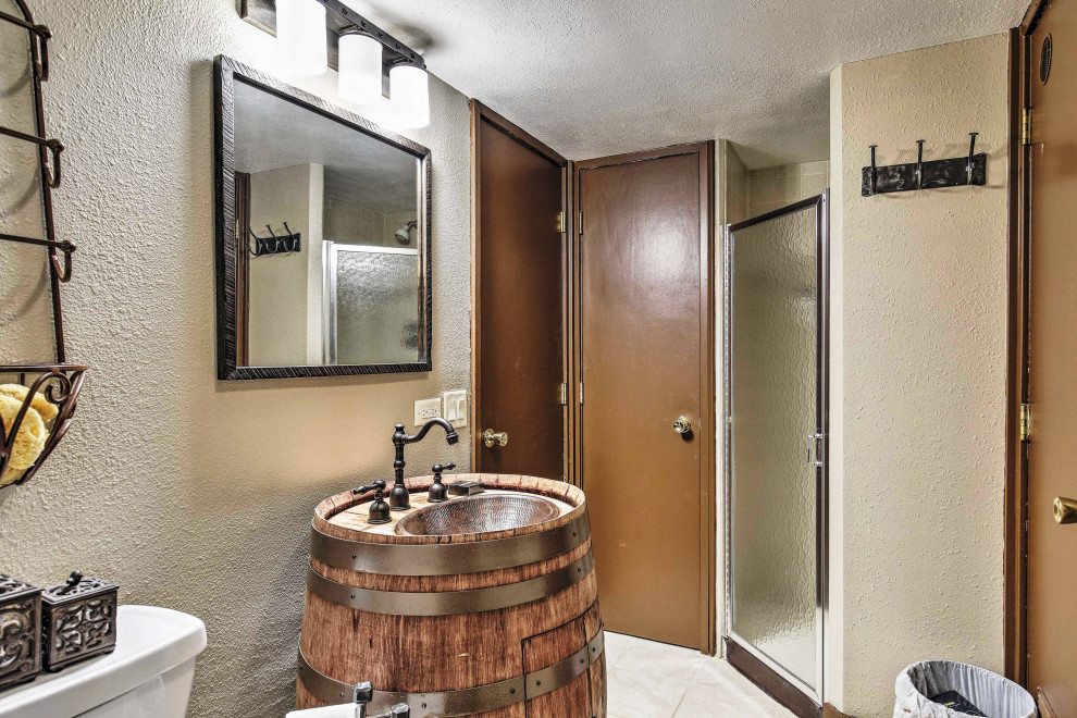 Пример оригинального дизайна: маленькая ванная комната в стиле рустика с фасадами с выступающей филенкой, искусственно-состаренными фасадами, угловым душем, унитазом-моноблоком, бежевыми стенами, полом из керамической плитки, раковиной с пьедесталом, столешницей из дерева, бежевым полом, душем с распашными дверями и коричневой столешницей для на участке и в саду