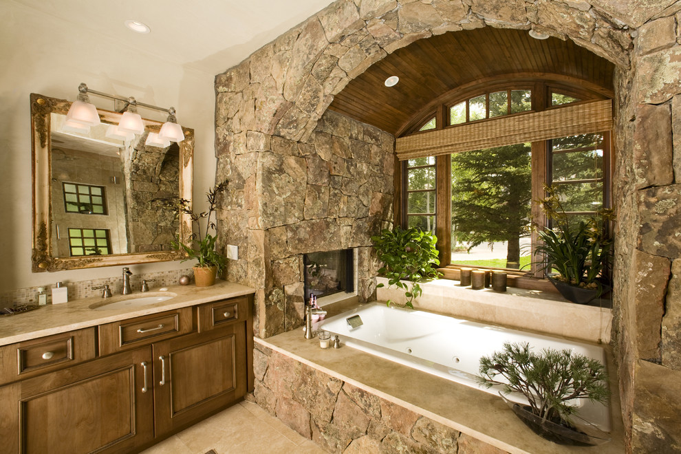 Immagine di una stanza da bagno rustica con lavabo sottopiano, ante con riquadro incassato, ante in legno scuro, vasca da incasso e piastrelle beige
