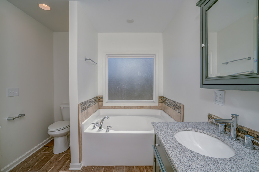 Large traditional ensuite bathroom in Nashville with freestanding cabinets, grey cabinets, an alcove bath, an alcove shower, a two-piece toilet, multi-coloured tiles, glass tiles, white walls, porcelain flooring, a submerged sink, granite worktops, brown floors and a hinged door.