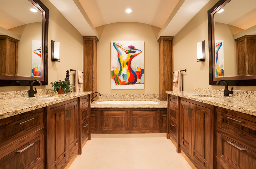 Cette image montre une grande salle de bain principale design en bois foncé avec un lavabo encastré, un placard à porte shaker, un plan de toilette en granite, une baignoire encastrée, un carrelage beige, des carreaux de porcelaine, un mur beige et un sol en carrelage de porcelaine.