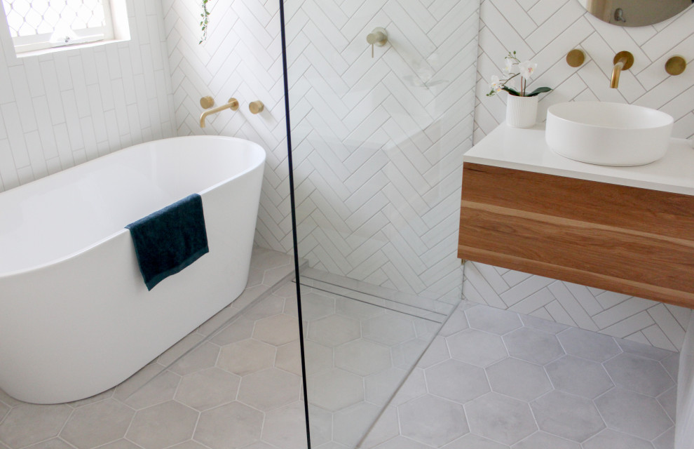 Пример оригинального дизайна: главная ванная комната среднего размера с плоскими фасадами, искусственно-состаренными фасадами, отдельно стоящей ванной, душевой комнатой, белой плиткой, керамической плиткой, белыми стенами, полом из мозаичной плитки, настольной раковиной, столешницей из искусственного кварца, серым полом, открытым душем, белой столешницей, тумбой под одну раковину и подвесной тумбой