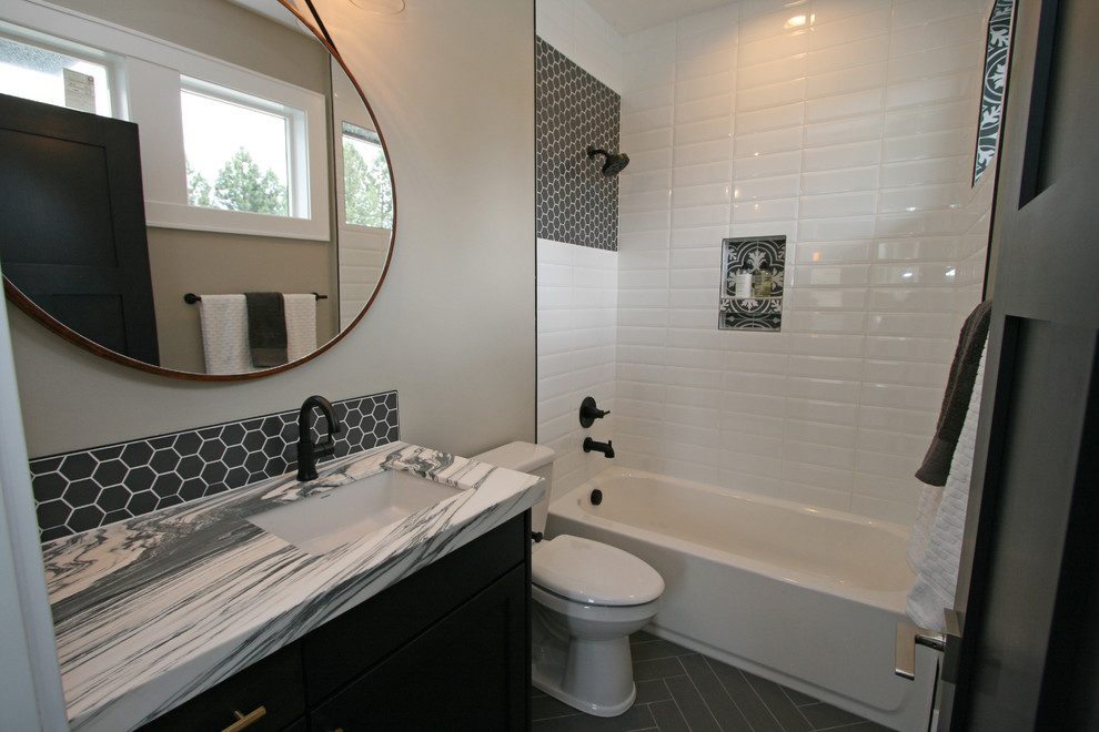 Photo of a small classic family bathroom in Seattle with shaker cabinets, black cabinets, an alcove bath, a shower/bath combination, a two-piece toilet, white tiles, porcelain tiles, grey walls, porcelain flooring, a submerged sink, marble worktops, black floors and white worktops.