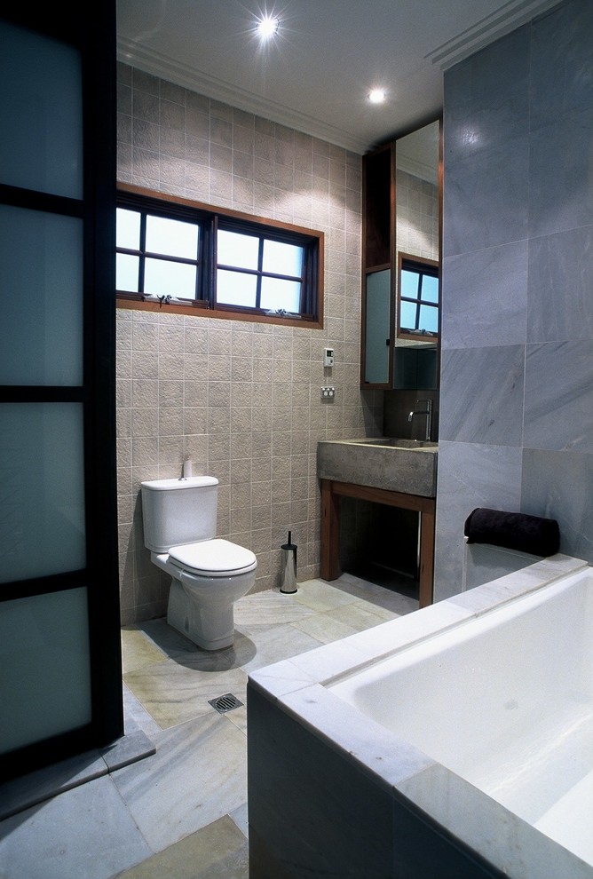 Corner shower - mid-sized modern master gray tile and stone tile limestone floor and gray floor corner shower idea in Sydney with glass-front cabinets, medium tone wood cabinets, a hot tub, a one-piece toilet, gray walls, a console sink, concrete countertops and a hinged shower door