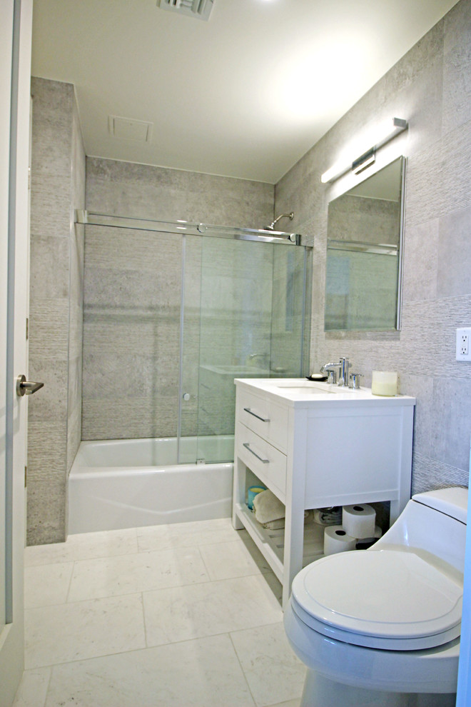 Foto på ett funkis badrum, med ett undermonterad handfat, vita skåp, bänkskiva i kvarts, ett badkar i en alkov, en dusch/badkar-kombination, en toalettstol med hel cisternkåpa, grå kakel, porslinskakel, grå väggar och klinkergolv i porslin