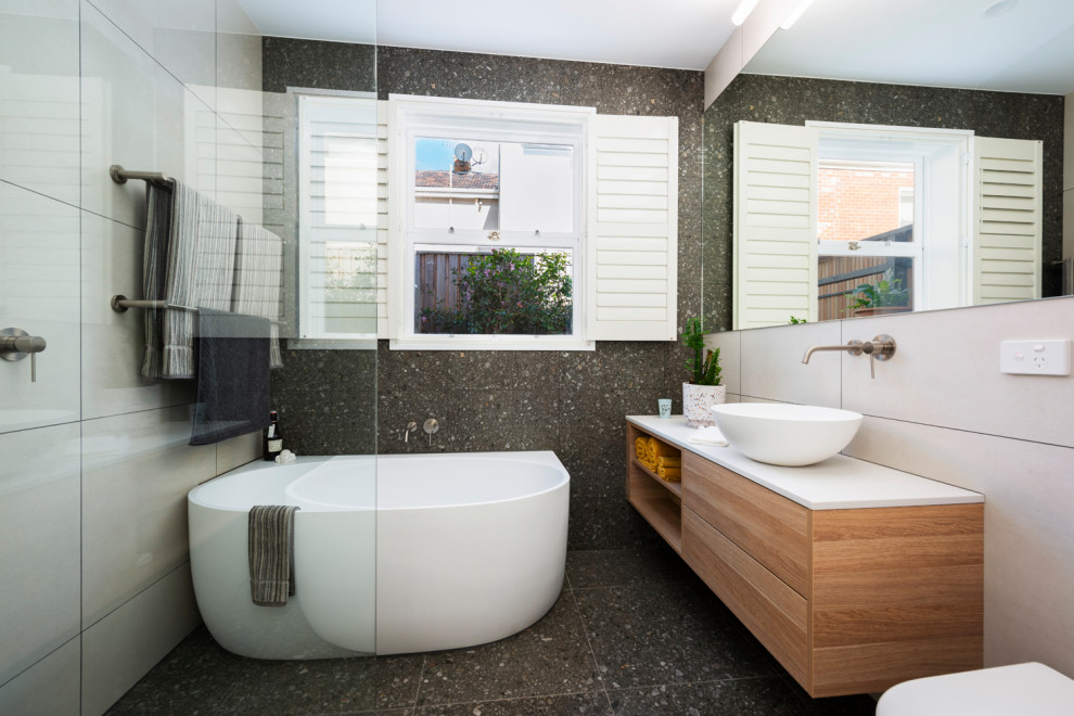 Пример оригинального дизайна: главная ванная комната среднего размера в современном стиле с фасадами цвета дерева среднего тона, отдельно стоящей ванной, открытым душем, инсталляцией, розовой плиткой, керамической плиткой, разноцветными стенами, полом из керамической плитки, настольной раковиной, столешницей из гранита, серым полом, открытым душем, белой столешницей, тумбой под одну раковину, подвесной тумбой и плоскими фасадами