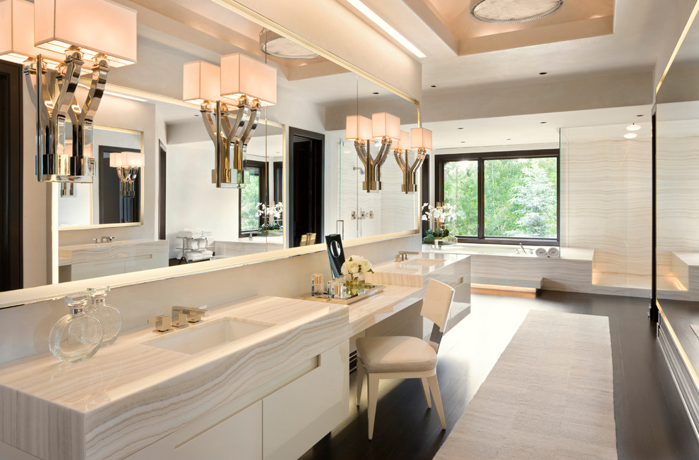 Inredning av ett modernt badrum, med ett undermonterad handfat, släta luckor, vita skåp, marmorbänkskiva, ett undermonterat badkar, en hörndusch och beige kakel