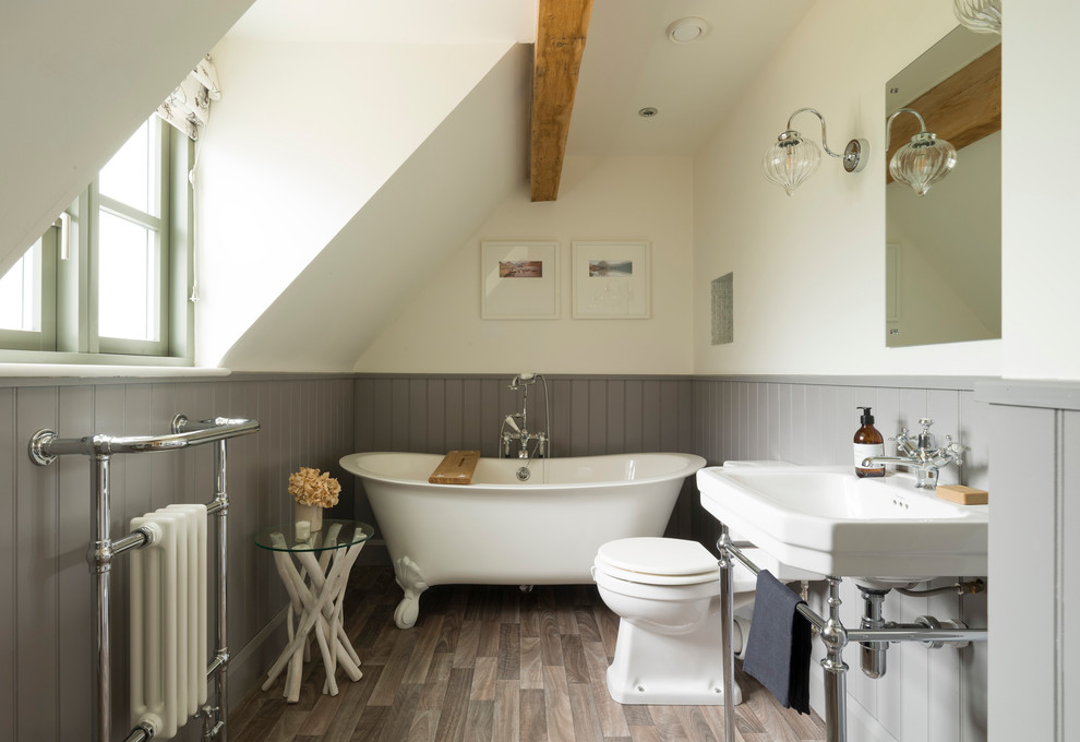 Landhausstil Duschbad mit Löwenfuß-Badewanne, Wandtoilette mit Spülkasten, weißer Wandfarbe, braunem Holzboden, Waschtischkonsole und braunem Boden in West Midlands