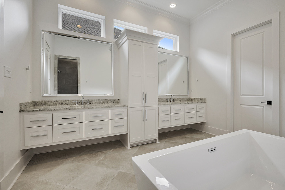 Klassisk inredning av ett mellanstort flerfärgad flerfärgat en-suite badrum, med luckor med infälld panel, vita skåp, ett fristående badkar, en dusch i en alkov, en toalettstol med separat cisternkåpa, grå kakel, skifferkakel, vita väggar, klinkergolv i porslin, ett undermonterad handfat, granitbänkskiva, beiget golv och dusch med gångjärnsdörr
