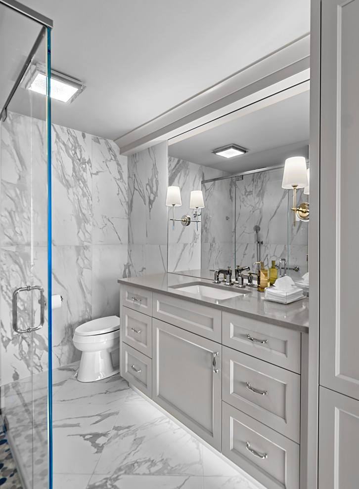 Пример оригинального дизайна: главная, серо-белая ванная комната среднего размера: освещение в стиле неоклассика (современная классика) с фасадами с утопленной филенкой, серыми фасадами, душем в нише, унитазом-моноблоком, белой плиткой, керамогранитной плиткой, серыми стенами, полом из керамогранита, врезной раковиной, столешницей из искусственного кварца, белым полом, душем с распашными дверями, серой столешницей, тумбой под одну раковину и подвесной тумбой