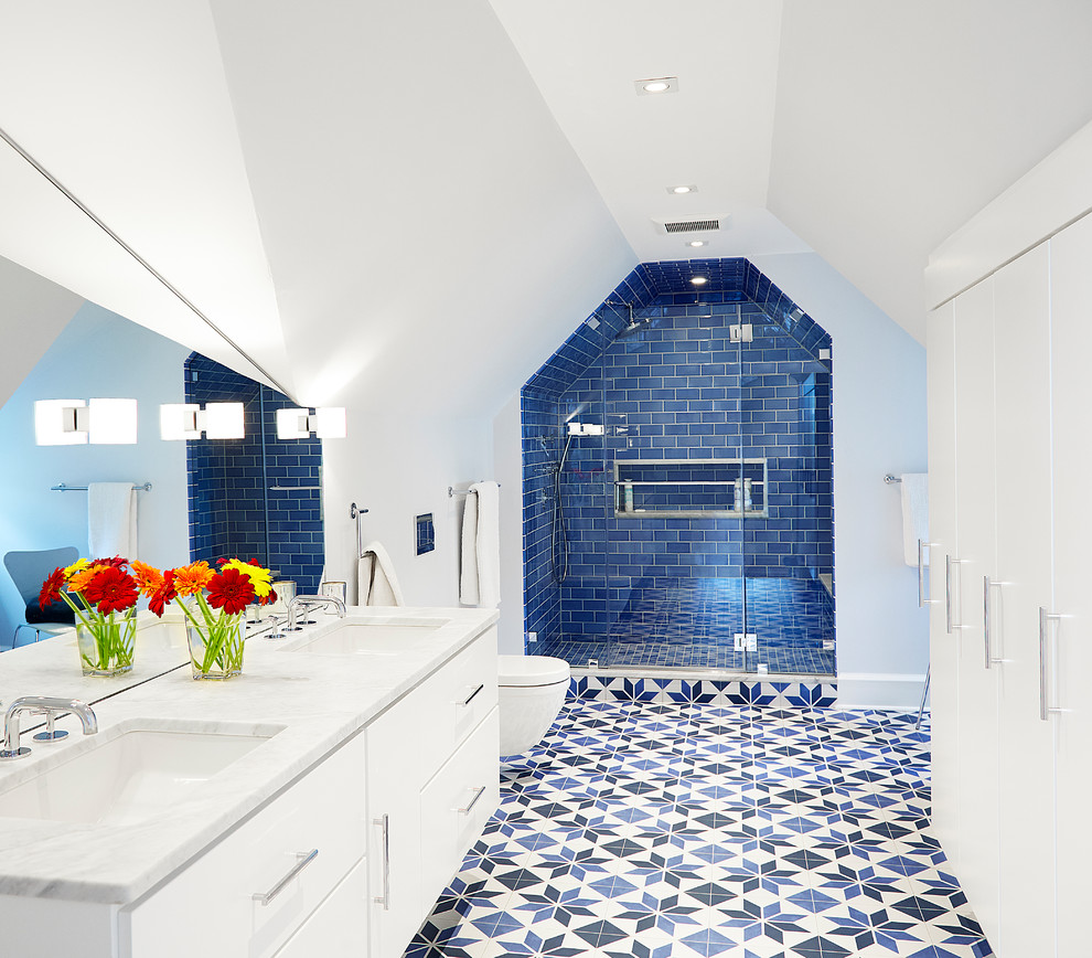 Inredning av ett modernt stort vit vitt badrum för barn, med släta luckor, vita skåp, en dusch i en alkov, en vägghängd toalettstol, blå kakel, keramikplattor, vita väggar, klinkergolv i porslin, ett undermonterad handfat, marmorbänkskiva, blått golv och dusch med gångjärnsdörr