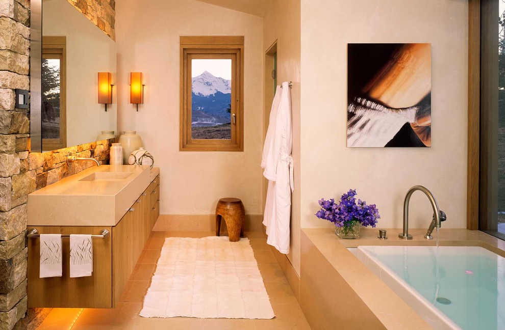 Rustikales Badezimmer mit integriertem Waschbecken, flächenbündigen Schrankfronten, hellbraunen Holzschränken, Einbaubadewanne, beigen Fliesen, beigem Boden und Steinwänden in Denver
