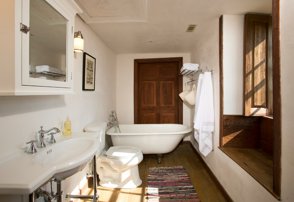 Foto på ett mellanstort lantligt badrum med dusch, med ett konsol handfat, ett badkar med tassar, en toalettstol med separat cisternkåpa, vita väggar och mellanmörkt trägolv