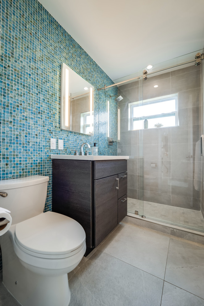 Idée de décoration pour une salle de bain minimaliste en bois foncé de taille moyenne avec un placard à porte plane, WC à poser, un carrelage bleu, des plaques de verre, un mur gris, un sol en carrelage de porcelaine, un lavabo encastré, un plan de toilette en quartz modifié, un sol gris, une cabine de douche à porte coulissante, un plan de toilette gris, meuble simple vasque et meuble-lavabo sur pied.