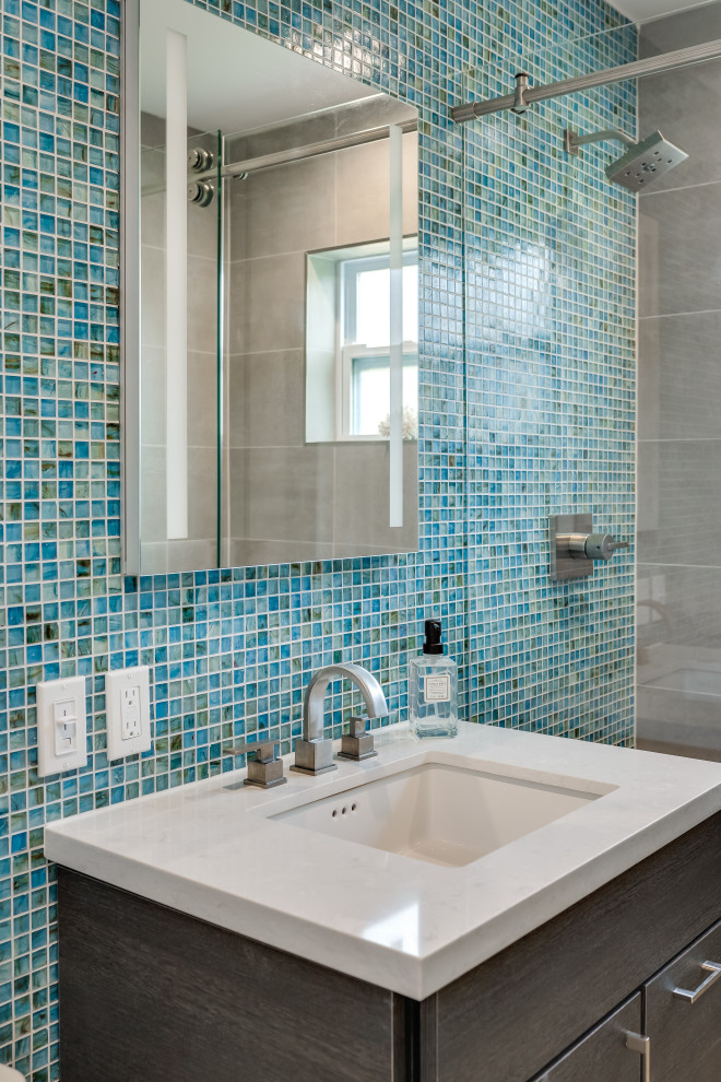 Exemple d'une salle de bain moderne en bois foncé de taille moyenne avec un placard à porte plane, WC à poser, un carrelage bleu, des plaques de verre, un mur gris, un sol en carrelage de porcelaine, un lavabo encastré, un plan de toilette en quartz modifié, un sol gris, une cabine de douche à porte coulissante, un plan de toilette gris, meuble simple vasque et meuble-lavabo sur pied.