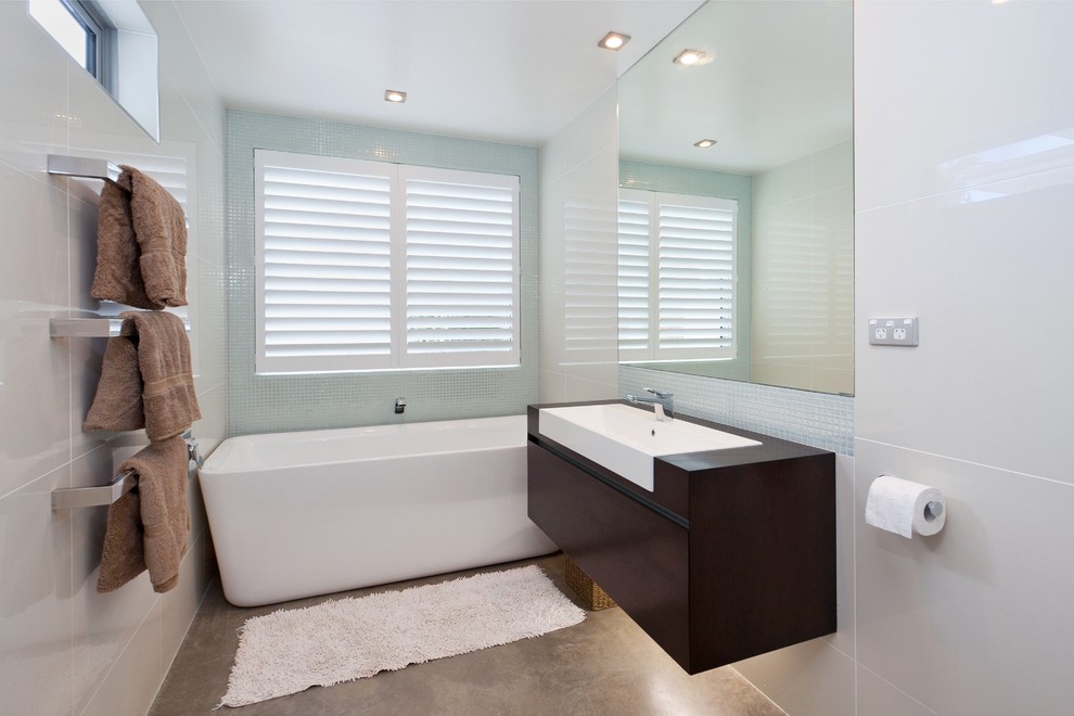 На фото: главная ванная комната среднего размера в современном стиле с плоскими фасадами, темными деревянными фасадами, отдельно стоящей ванной, серой плиткой, керамической плиткой, серыми стенами, бетонным полом, накладной раковиной и столешницей из дерева