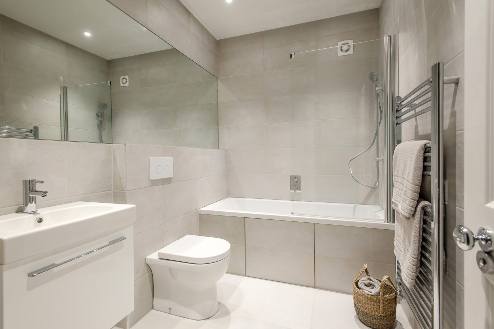 Small contemporary family bathroom in London with freestanding cabinets, white cabinets, a built-in bath, a shower/bath combination, a one-piece toilet, grey tiles, ceramic tiles, grey walls, ceramic flooring, a built-in sink and white floors.