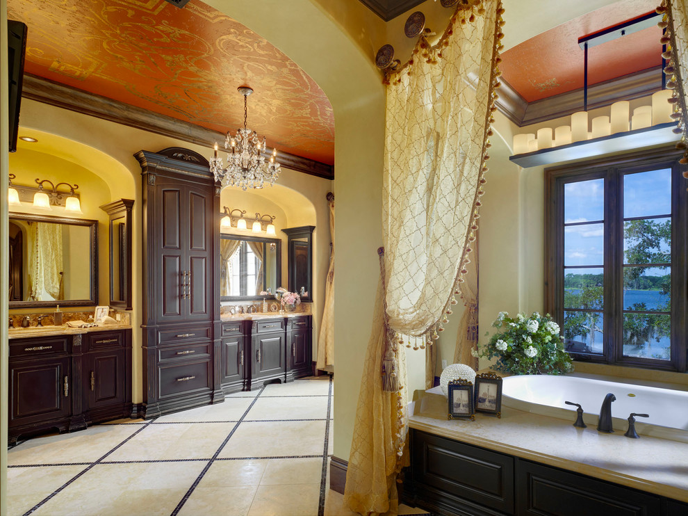 Photo of a large mediterranean ensuite bathroom in Orlando with raised-panel cabinets, dark wood cabinets, a built-in bath, beige tiles, travertine tiles, green walls and travertine flooring.