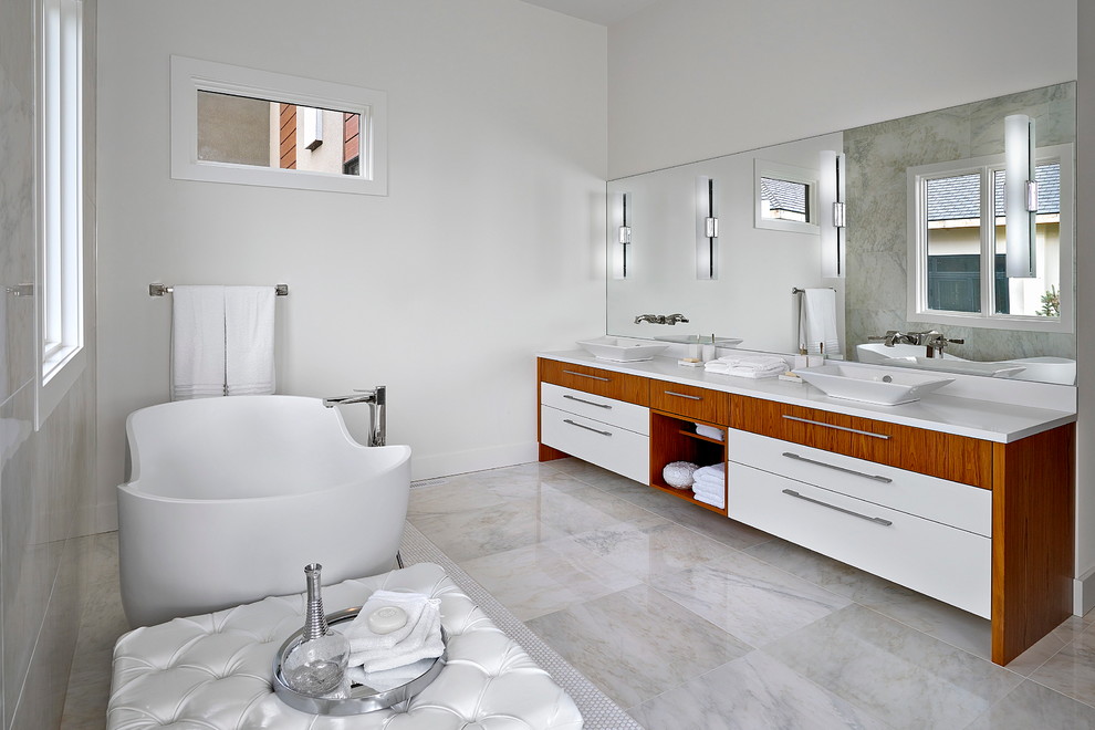 Idée de décoration pour une grande salle de bain principale design avec une vasque, un placard à porte plane, des portes de placard blanches, un plan de toilette en quartz, une baignoire indépendante, un mur blanc et un sol en carrelage de porcelaine.
