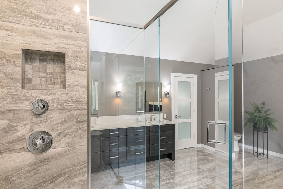 Inspiration for a large contemporary ensuite bathroom in Boston with flat-panel cabinets, dark wood cabinets, a freestanding bath, a built-in shower, a two-piece toilet, grey tiles, porcelain tiles, grey walls, porcelain flooring, a submerged sink, engineered stone worktops, grey floors, a hinged door and white worktops.