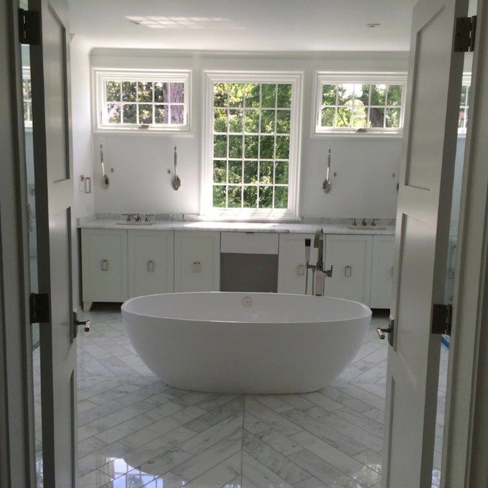 Cette image montre une grande douche en alcôve principale design avec un placard avec porte à panneau encastré, des portes de placard blanches, une baignoire indépendante, un carrelage gris, un carrelage blanc, un carrelage de pierre, un mur blanc, un sol en marbre, un lavabo encastré, un plan de toilette en marbre et un sol gris.