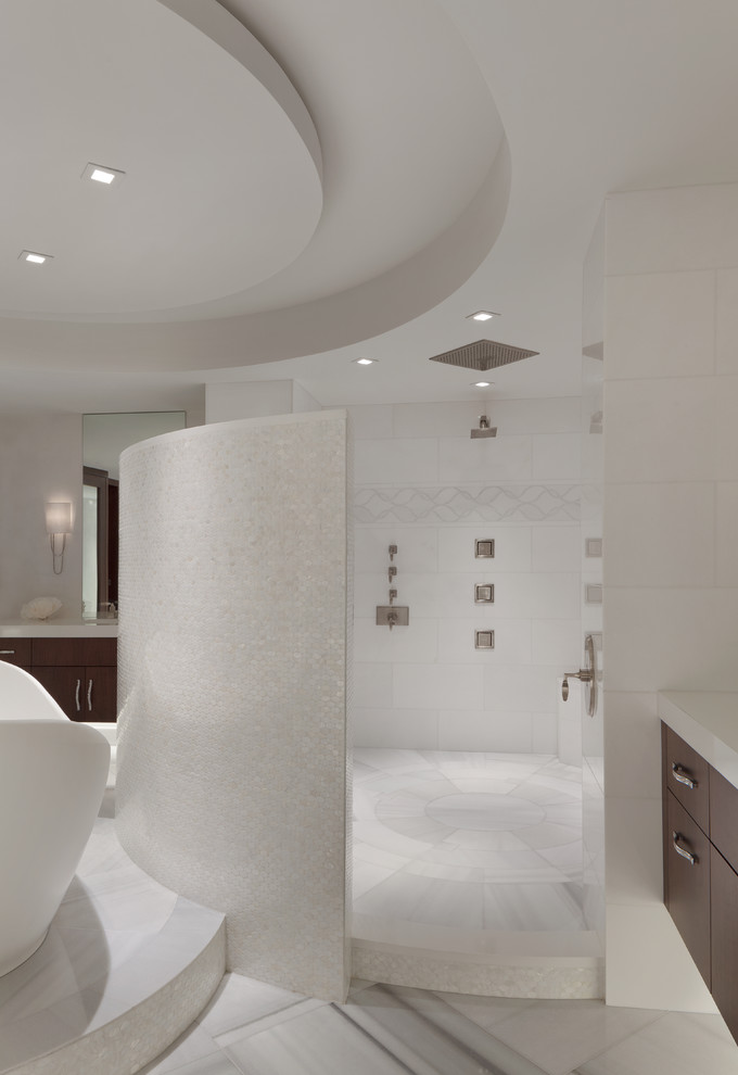 Photo of a large contemporary ensuite bathroom in Miami with flat-panel cabinets, dark wood cabinets, a freestanding bath, a double shower, white tiles, stone tiles, white walls, ceramic flooring, a submerged sink and marble worktops.