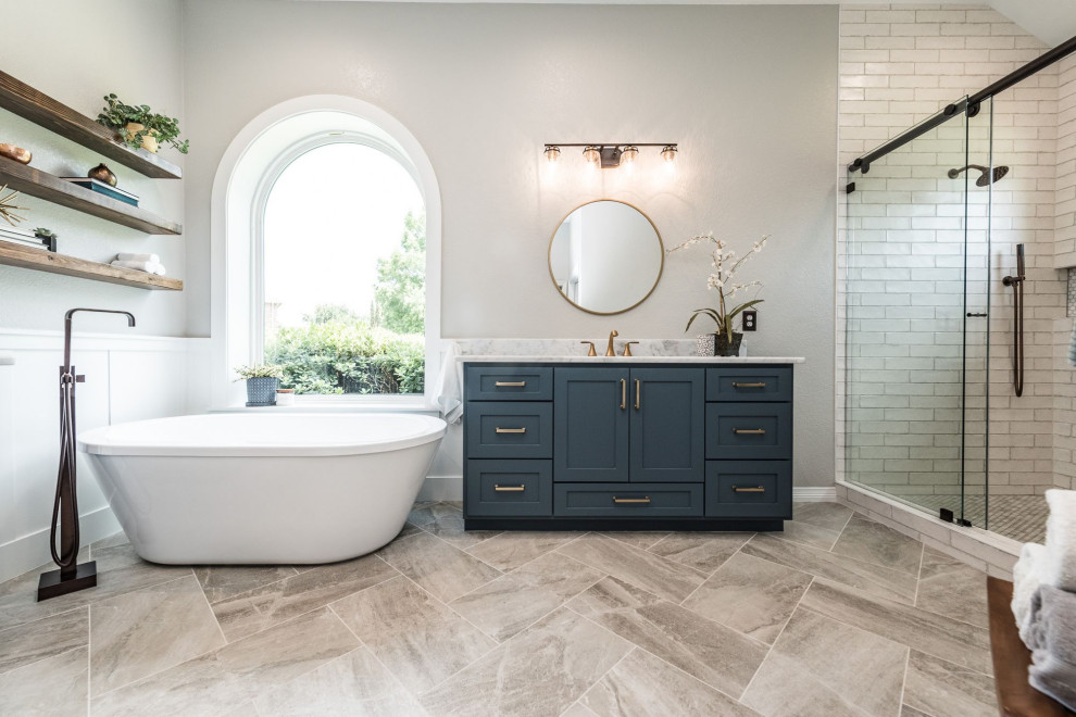 This is an example of a large traditional ensuite bathroom in Dallas with shaker cabinets, blue cabinets, a freestanding bath, an alcove shower, white tiles, ceramic tiles, grey walls, porcelain flooring, a submerged sink, marble worktops, multi-coloured floors, a sliding door and white worktops.